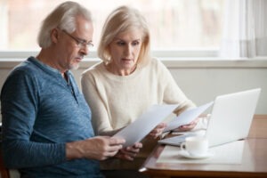 An elderly couple reviews financial documents in front of an open laptop. An investment fraud lawyer can explain how FINRA Rule 3210 impacts your case.