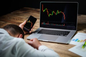 Person with their head on a table with charts in front of them that show their cryptocurrency losses and thinking about the type of attorney they need to recover their crypto losses