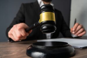Person in a dark suit raising a black and gold gavel over its sound block, with a pen and papers on a wooden desk
