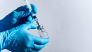 Gloved hands drawing clear medication from a glass vial into a syringe