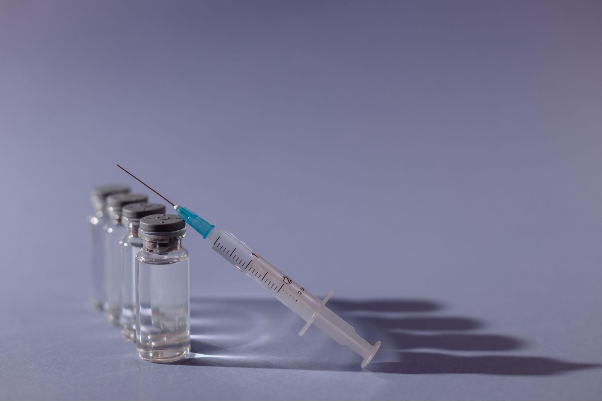 Syringe with a blue needle cap resting against a row of glass medication vials