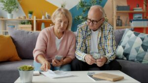 Senior couple sitting on a couch reviewing bills and counting cash together