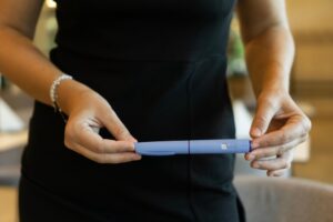 Woman in a black dress holding a blue medication injection pen in both hands
