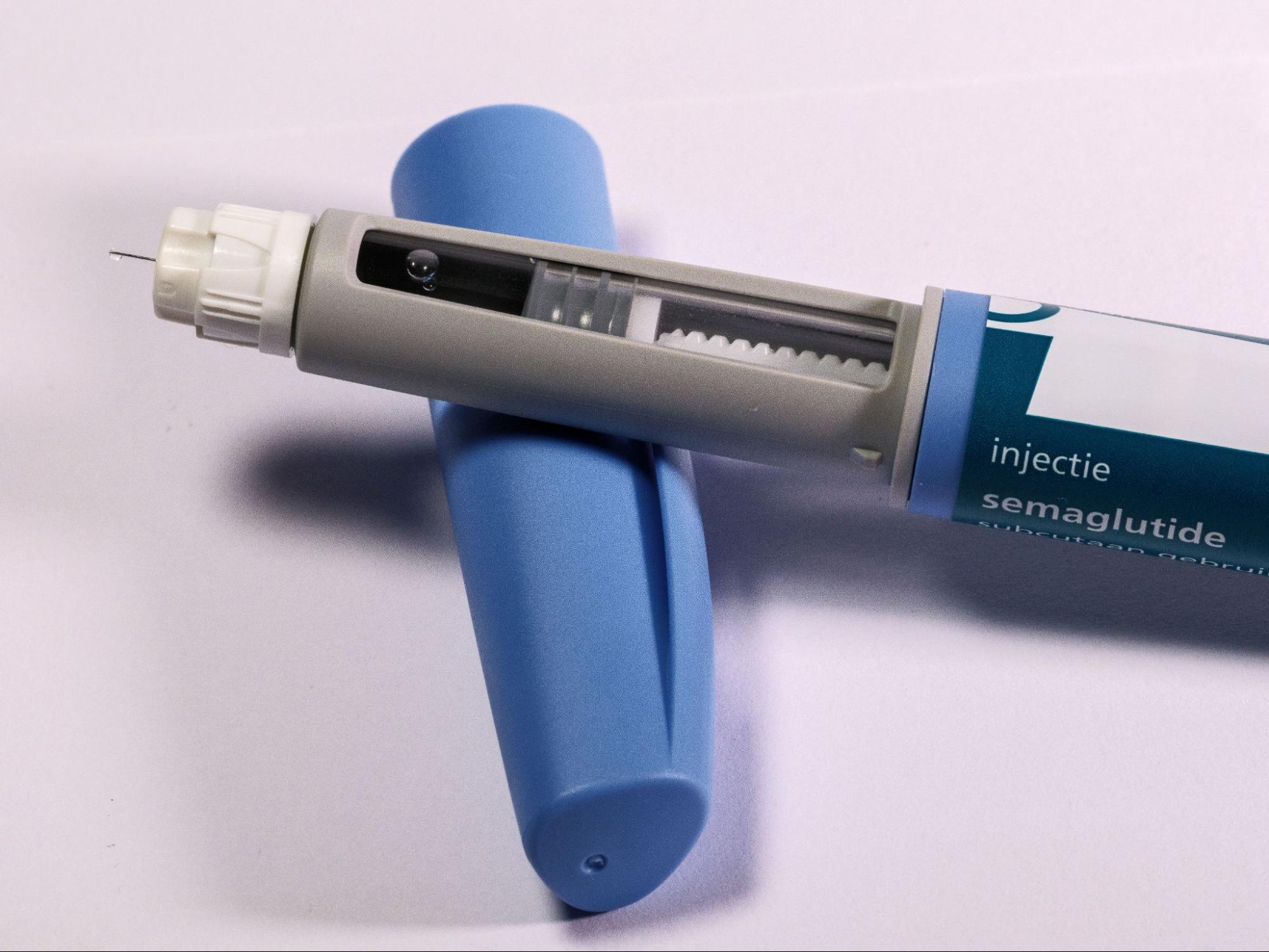 Semaglutide injection pen with a needle attached and its blue cap removed, lying on a white surface