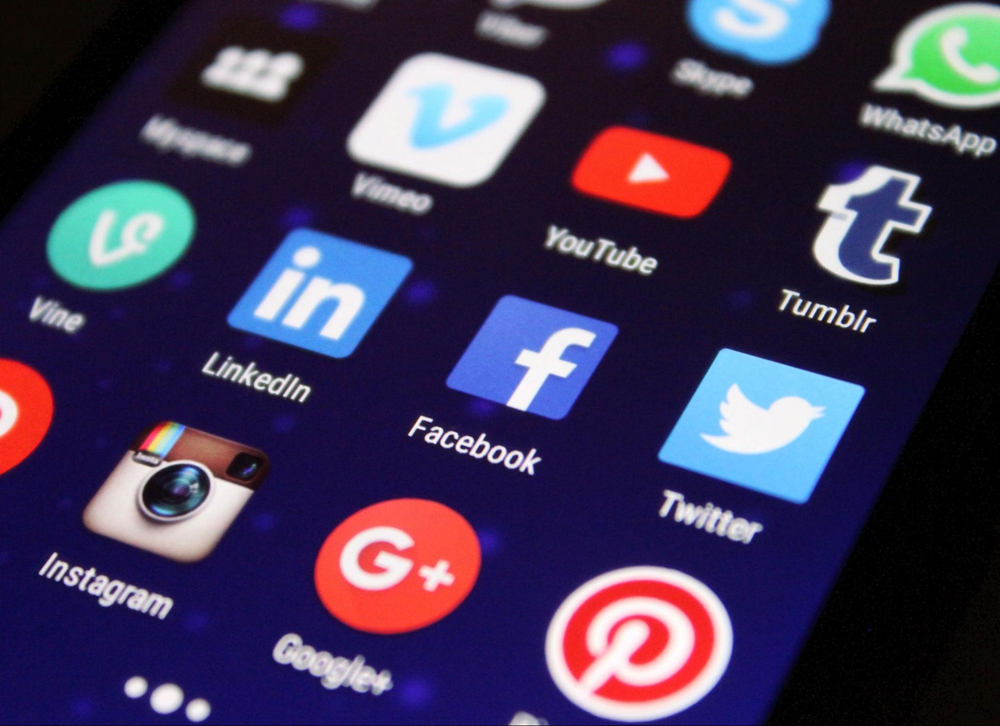 Close up of a smartphone screen showing social media app icons including Facebook, Instagram, YouTube, Twitter, and LinkedIn