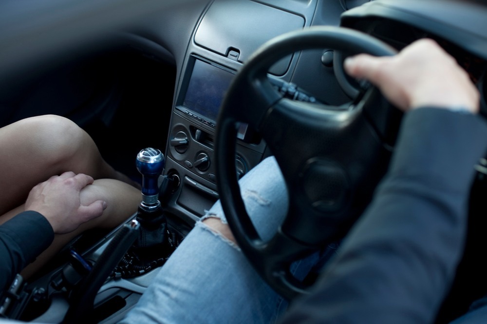 Driver resting his hand on the bare knee of a passenger in the front seat while his other hand holds the steering wheel